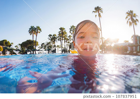 Girl learning to swim in the pool during summer vacation. Beach resort vacation by sea. Winter or summer seaside resort holiday. 107837951