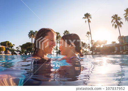 Mother teaching daughter to swim in pool during summer vacation. Mother and daughter playing in water. Beach resort vacation by the sea. Winter or summer seaside holiday. Mother teaching daughter to swim in pool during summer vacation. Mother and daughter playing in water. Beach resort vacation by the sea. Winter or summer seaside holiday. 107837952