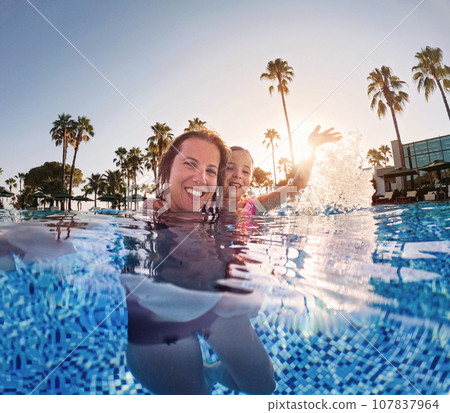 Mother teaching daughter to swim in pool during summer vacation. Mother and daughter playing in water. Beach resort vacation by the sea. Winter or summer seaside holiday. 107837964