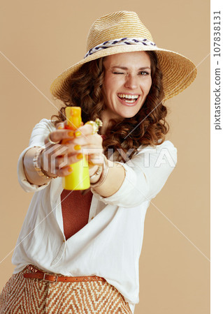 smiling stylish housewife aiming as gun isolated on beige 107838131