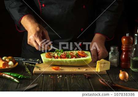 The cook adds green parsley to the zucchini. The concept of cooking a national stuffed squash boat or marrow in a restaurant kitchen 107838386