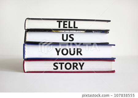 Tell us your story symbol. Books with words 'Tell us your story'. Businessman hand. Beautiful white background, copy space. Business, storytelling and tell us your story concept. Tell us your story symbol. Books with words 'Tell us your story'. Businessman hand. Beautiful white background, copy space. Business, storytelling and tell us your story concept. 107838555