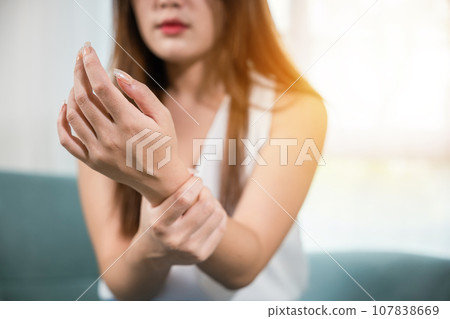 Closeup hand. Asian woman hand problem injury feeling joint pain, young female sitting on sofa holds suffering her wrist at home, performing self-massage, Health care and medical concept Closeup hand. Asian woman hand problem injury feeling joint pain, young female sitting on sofa holds suffering her wrist at home, performing self-massage, Health care and medical concept 107838669