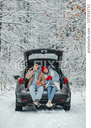 A couple in a snowy forest stopped for a drink and snack and a rest from the road A couple in a snowy forest stopped for a drink and snack and a rest from the road 107838732