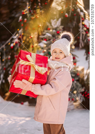 Little girl with a big Christmas gift outdoors in winter on Christmas Eve. Little girl with a big Christmas gift outdoors in winter on Christmas Eve. 107838789