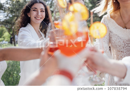 Close up of young women holding elegant glasses with long stem of alcohol cocktails and clink them. Close up of young women holding elegant glasses with long stem of alcohol cocktails and clink them. 107838794