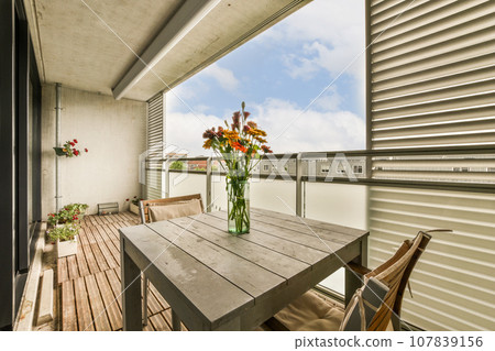 some flowers in a vase on a wooden table with a view of the sky and clouds behind it from an apartment balcony 107839156