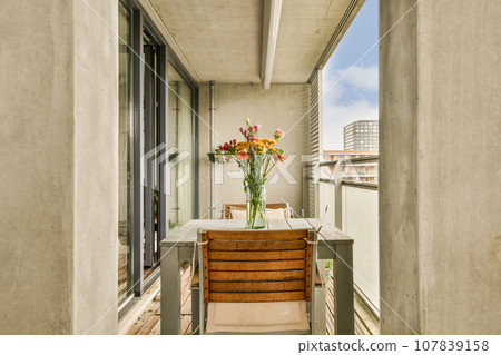 a balcony with flowers in a vase on the table next to an open patio door that leads out onto the street 107839158