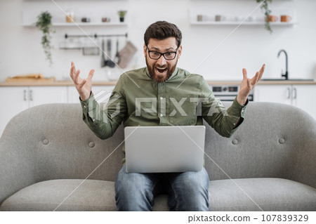 Confused male shrugging shoulders with laptop on couch Confused male shrugging shoulders with laptop on couch 107839329