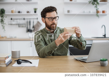 Man experiencing pleasant shock while unpacking parcel box Man experiencing pleasant shock while unpacking parcel box 107839421