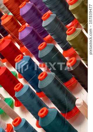 Row of multicolored thread spools at sewing factory Row of multicolored thread spools at sewing factory 107839477