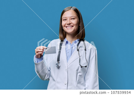Young woman medical specialist, doctor holding bank credit card on blue background Young woman medical specialist, doctor holding bank credit card on blue background 107839934