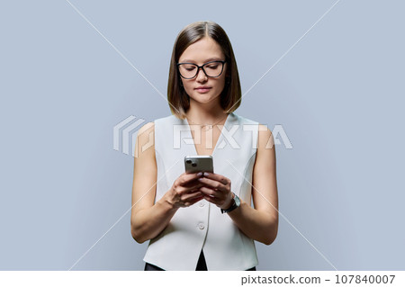 Young confident woman with smartphone in hands on gray studio background 107840007