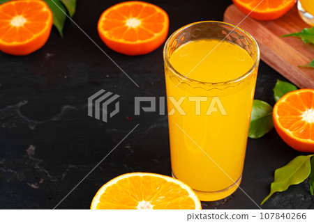 Glass of orange juice and cut oranges on table Glass of orange juice and cut oranges on table 107840266