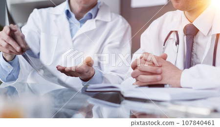 Two doctors look at x-rays and discuss the diagnosis. They sit a 107840461