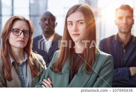 Young executive smiling and standing in a bright room with her team behind her 107840836