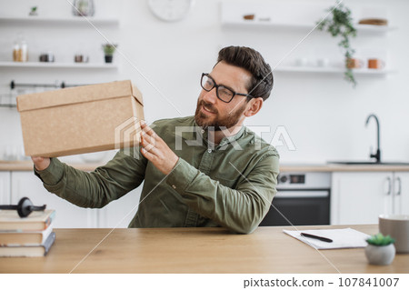 Excited blogger sitting at desk with cardboard box in hands Excited blogger sitting at desk with cardboard box in hands 107841007