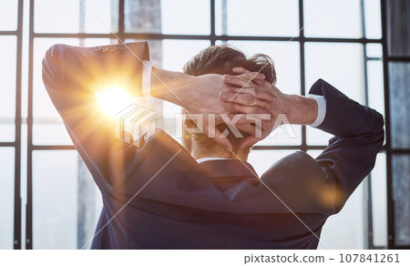 worker sitting in office with hands behind his head worker sitting in office with hands behind his head 107841261