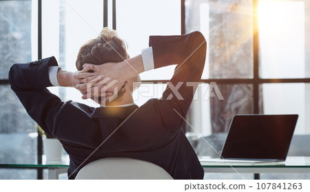 worker sitting in office with hands behind his head 107841263