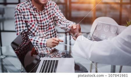 Doctor and patient shaking hands in the office, they are sitting at desk 107841981