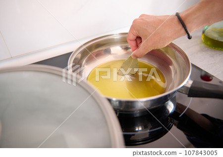 Close-up of a man's hand holding a bay leaf and seasoning the olive oil frying in a pan while cooking dinner at home Close-up of a man's hand holding a bay leaf and seasoning the olive oil frying in a pan while cooking dinner at home 107843005