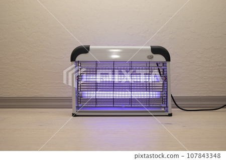 Electric Mosquito and Insect Zapper With Blue Purple Lights Turned on. Bug Killer Lamp on Wooden Floor in Room. Fly Trap for Outdoor and Indoor. Horizontal Plane  107843348
