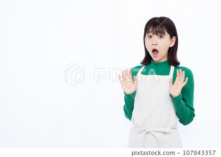 A housewife in her 30s looking surprised in front of a white background A housewife in her 30s looking surprised in front of a white background 107843357