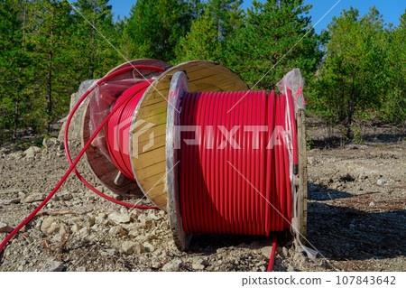 Wooden Reel with High Voltage Red Cable in Forest: Ready for Underground Power Line Installation Wooden Reel with High Voltage Red Cable in Forest: Ready for Underground Power Line Installation 107843642