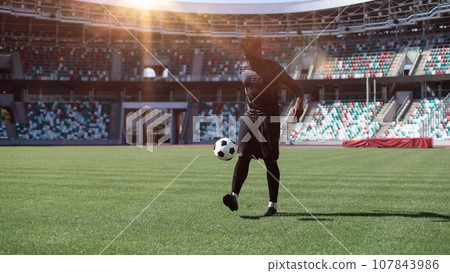African American man playing football on the stadium field. A man runs with a soccer ball across the field. 107843986