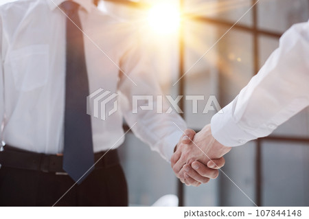 Two businessmen shake hands on the background of empty modern office, signing of a contract concept, close up Two businessmen shake hands on the background of empty modern office, signing of a contract concept, close up 107844148
