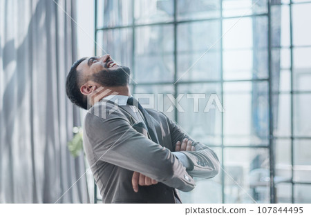 A joyful businessman standing with hands raised in victory and looking up A joyful businessman standing with hands raised in victory and looking up 107844495