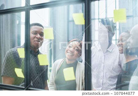 a team of young designers sticking notes on glass in a modern office a team of young designers sticking notes on glass in a modern office 107844877