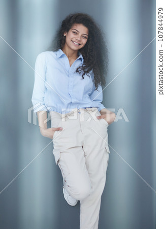 Smiling attractive young business woman in blue shirt posing on gray background 107844979