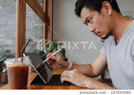 Serious freelance man working in the cafe with his tablet computer. 107845060