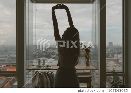 Woman stretching lazily by the windows in her apartment in a relax day. Woman stretching lazily by the windows in her apartment in a relax day. 107845085