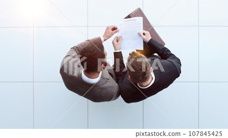 Two businessman signing an agreement. One hand holds the document and the other signs. Two businessman signing an agreement. One hand holds the document and the other signs. 107845425