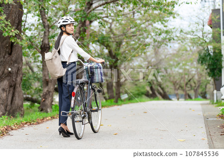A young woman wearing a cycling helmet and walking with a bicycle A young woman wearing a cycling helmet and walking with a bicycle 107845536