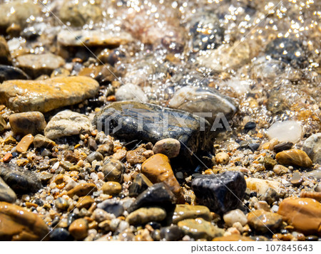Close-up of the waves on a stony sandy beach. 107845643