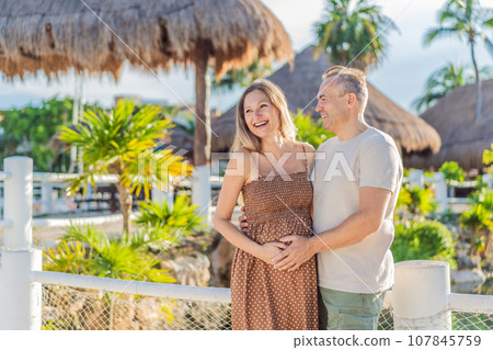 A happy, mature couple over 40, enjoying a leisurely walk in a park, their joy evident as they embrace the journey of pregnancy later in life A happy, mature couple over 40, enjoying a leisurely walk in a park, their joy evident as they embrace the journey of pregnancy later in life 107845759