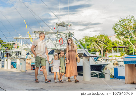 A happy, mature couple over 40 with their two daughters enjoying a leisurely walk on the waterfront, their joy evident as they embrace the journey of pregnancy later in life A happy, mature couple over 40 with their two daughters enjoying a leisurely walk on the waterfront, their joy evident as they embrace the journey of pregnancy later in life 107845769