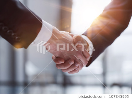 Businessmen shaking hands standing in front of office windows 107845995