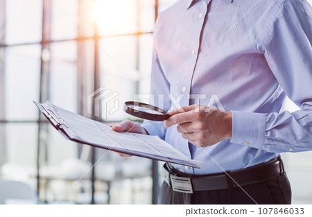 Businessman looking through a magnifying glass to documents 107846033