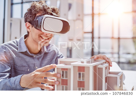 man sits in the office of a realtor and looks at the layout of the apartment in virtual reality glasses. man sits in the office of a realtor and looks at the layout of the apartment in virtual reality glasses. 107846830