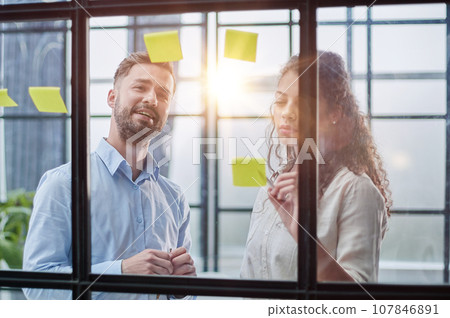 Business people talking in the hallway of the modern office building with employees working behind glass partitions. Work in a large business corporation 107846891