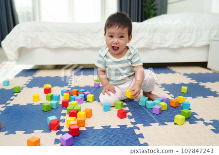 happy infant baby playing wooden block toy on jigsaw mat in bedroom 107847241