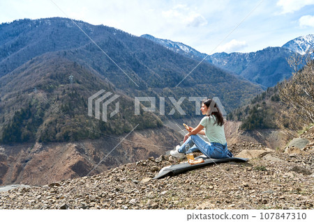A girl on a picnic with an incredible natural view of the mountains and a dehydrated mountain river. Gorgeous scenery 107847310