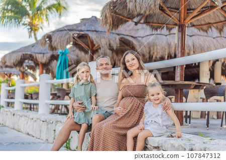 A happy, mature couple over 40 with their two daughters, enjoying a leisurely walk in a park, their joy evident as they embrace the journey of pregnancy later in life 107847312