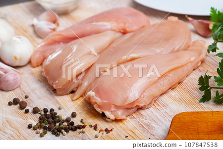 Preparation of raw chicken breast fillet with parsley and garlic on cutting board Preparation of raw chicken breast fillet with parsley and garlic on cutting board 107847538