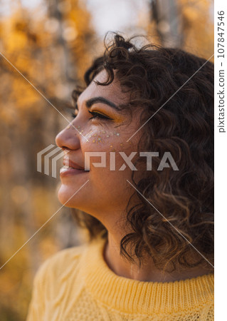 Curly girl smiling in a yellow knitted sweater in front of the forest Curly girl smiling in a yellow knitted sweater in front of the forest 107847546