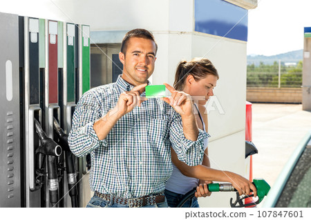Smiling man and woman in gas station, demonstrating gas credit card 107847601